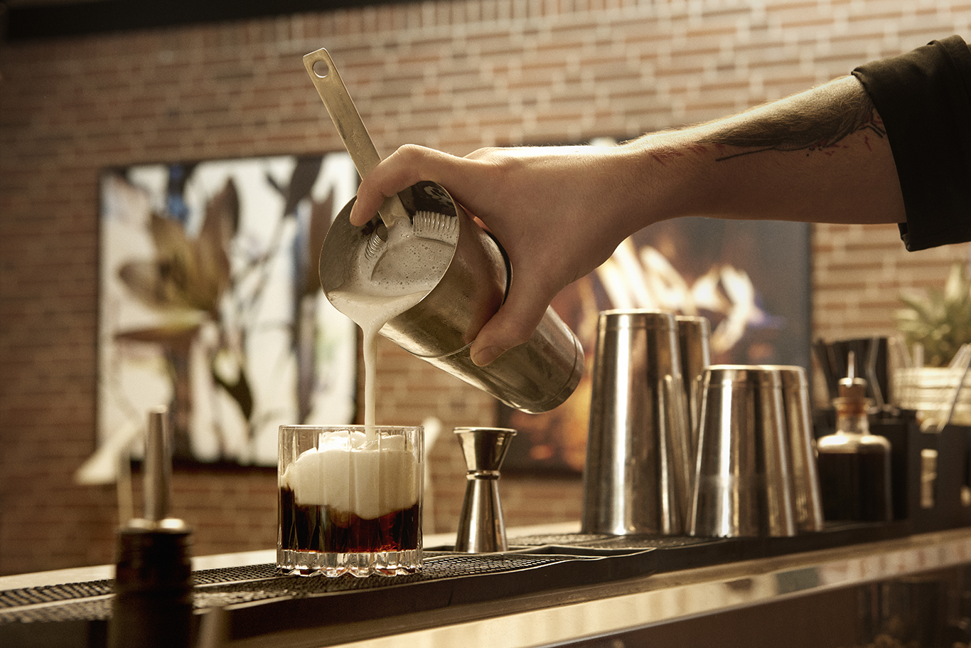 bartender skænker cocktail op fra cocktail shaker med skum i glasset